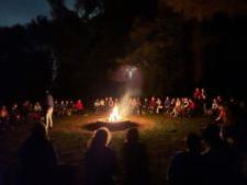 伦理文化学生，教师和工作人员聚集在篝火周围在晚上.